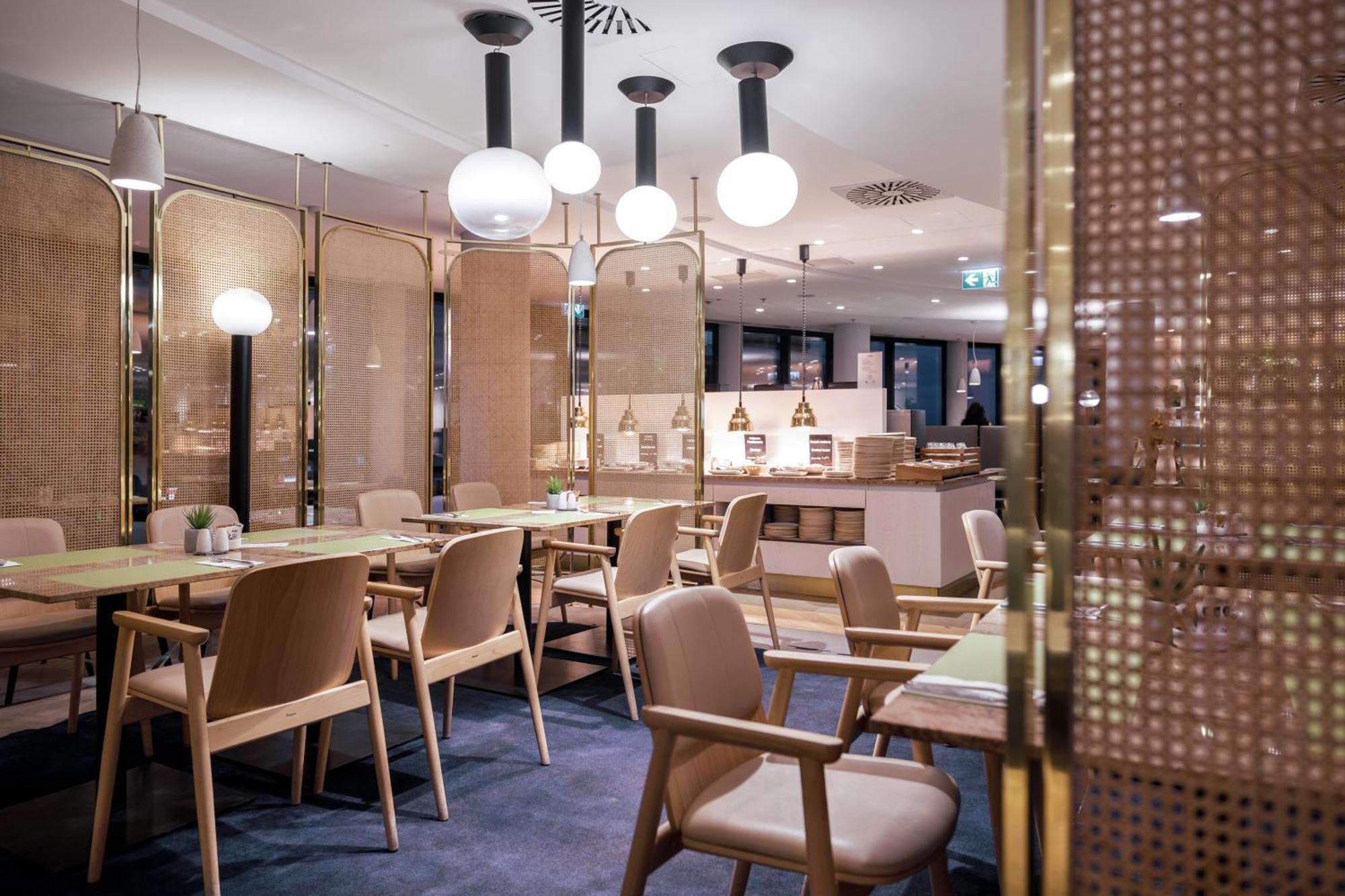 Radisson Blu Resort Świnoujście מראה חיצוני תמונה The photo shows a modern restaurant interior. There are wooden tables and chairs arranged neatly. The atmosphere appears warm and inviting, with soft lighting provided by round pendant lamps hanging from the ceiling. Partitions made of woven material