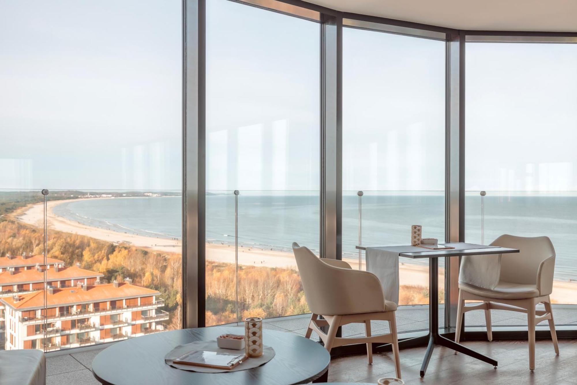 Radisson Blu Resort Świnoujście מראה חיצוני תמונה The photo shows a modern interior space with large floor-to-ceiling windows that provide a stunning view of the beach and sea. The area appears to be a dining or lounge space, featuring a minimalistic table and chairs. There is a sense of tranquility