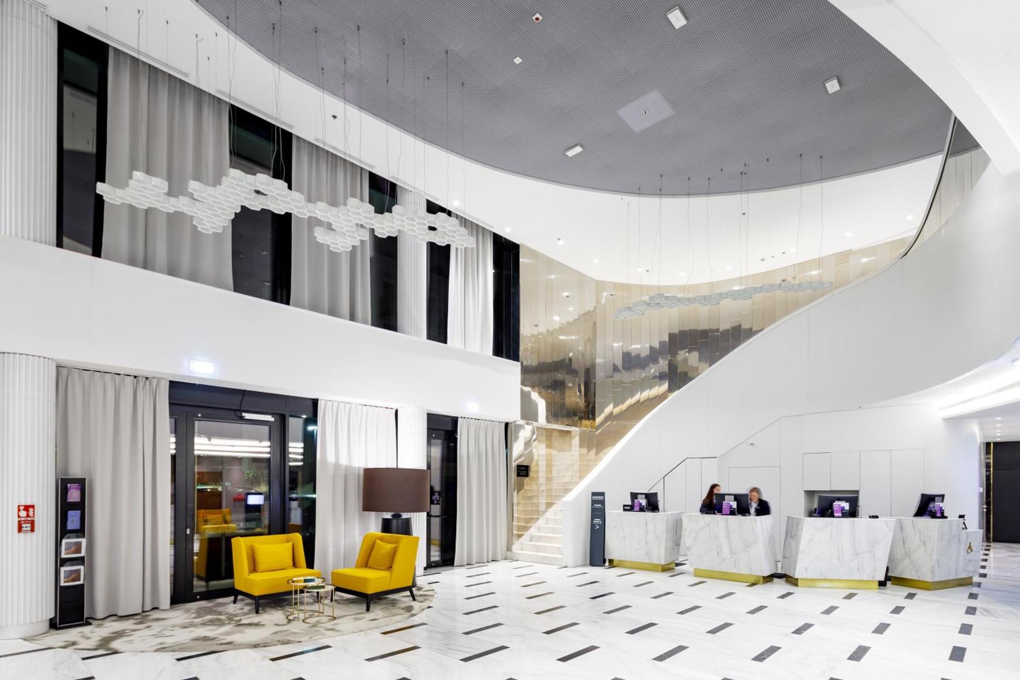 Radisson Blu Resort Świnoujście מראה חיצוני תמונה The photo shows a modern interior space, likely a hotel or a lobby area. It features a spacious, open design with high ceilings and a stylish staircase that leads to an upper level. The walls are mostly white, with large windows allowing natural ligh