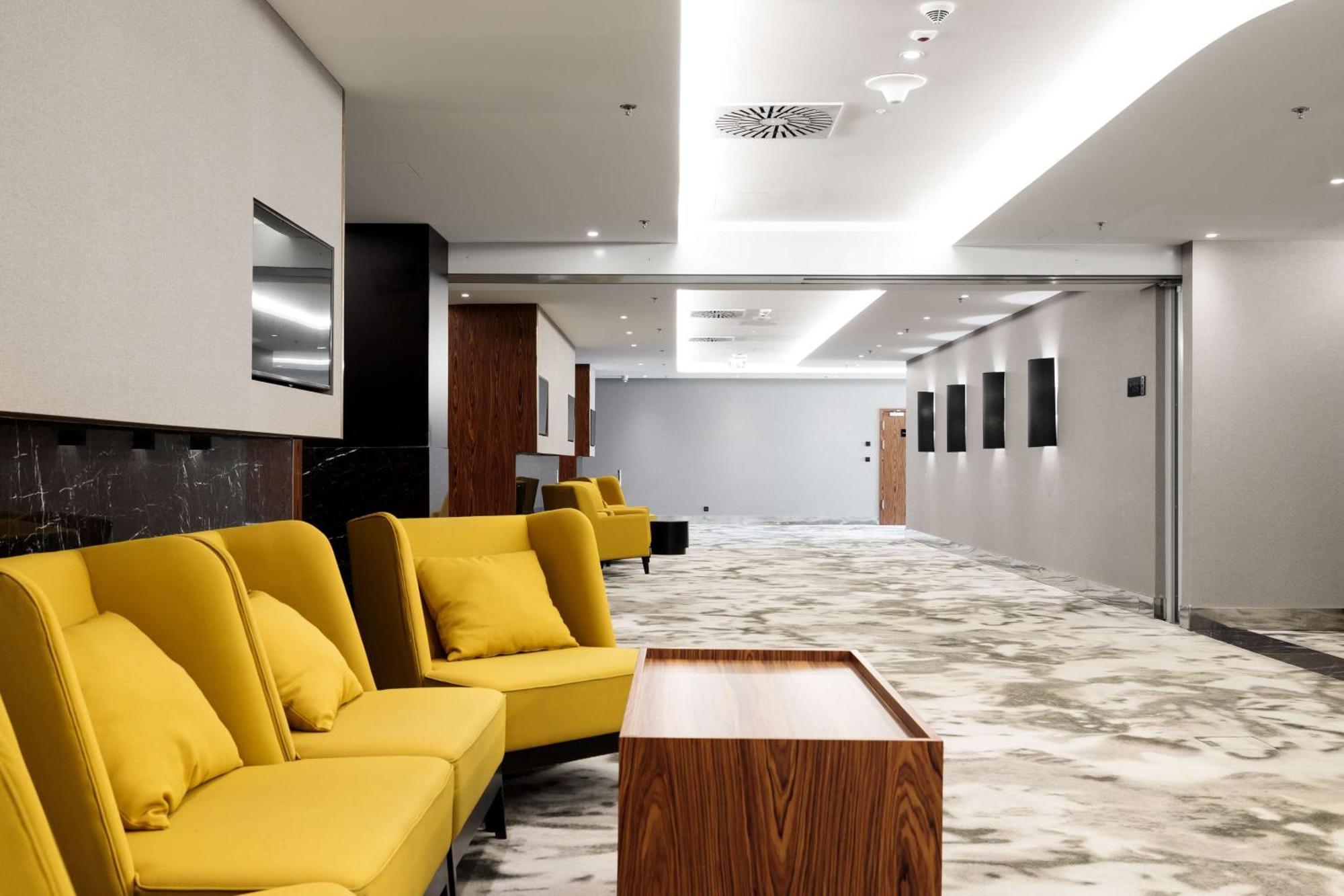 Radisson Blu Resort Świnoujście מראה חיצוני תמונה The photo shows a modern interior space, likely a lobby or waiting area. There are several yellow sofas with cushions arranged in a casual seating area. In front of the sofas, there is a wooden coffee table. The flooring features a gray and white mar