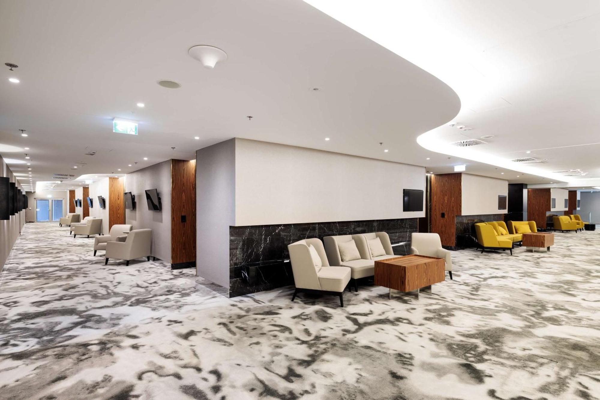 Radisson Blu Resort Świnoujście מראה חיצוני תמונה The photo shows a modern interior space, likely a lobby or lounge area. The flooring features a patterned carpet, and the walls are neutral in color, creating a calm ambiance. There are comfortable seating arrangements, including a group of beige cha