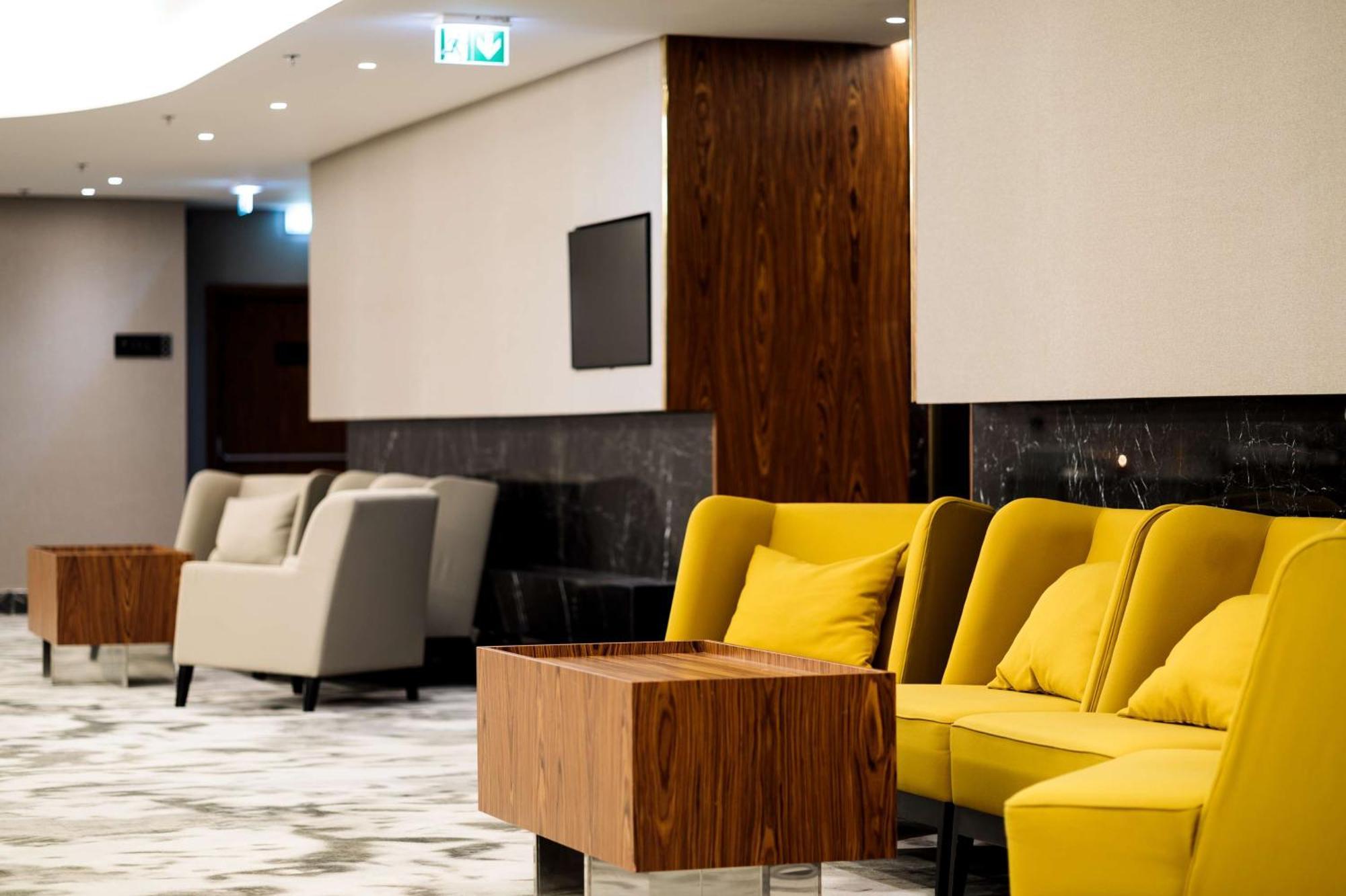 Radisson Blu Resort Świnoujście מראה חיצוני תמונה The photo depicts a modern lounge or waiting area with stylish seating. On the left, there are soft gray armchairs arranged around a wooden coffee table. In the center, there are yellow chairs with plush cushions, contributing a vibrant contrast to t