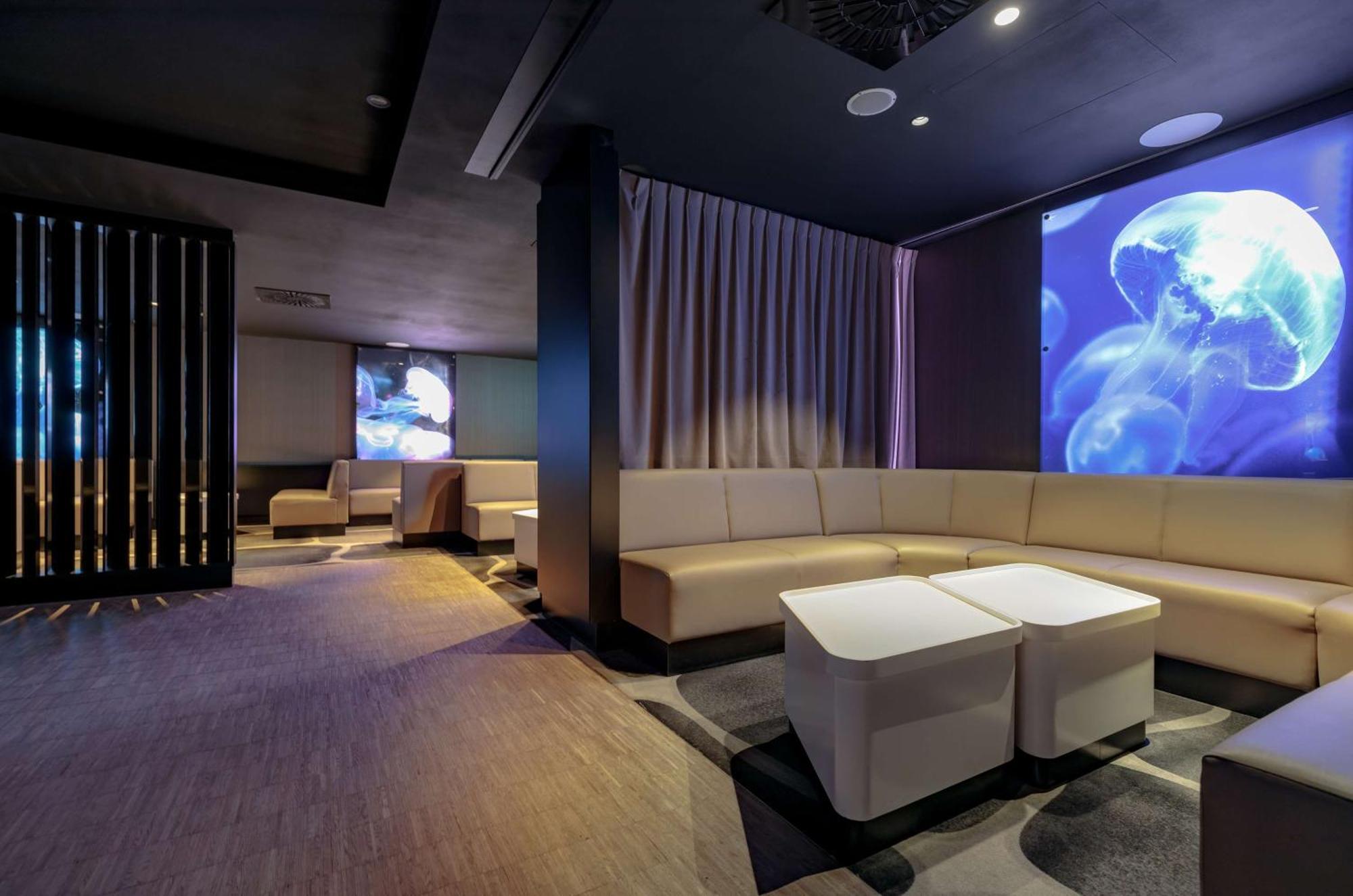 Radisson Blu Resort Świnoujście מראה חיצוני תמונה The photo shows a modern interior space that appears to be a lounge or relaxation area. The design is sleek and minimalist, featuring a curved, light-colored seating arrangement with low tables at the center. The walls are dark, contributing to a coz
