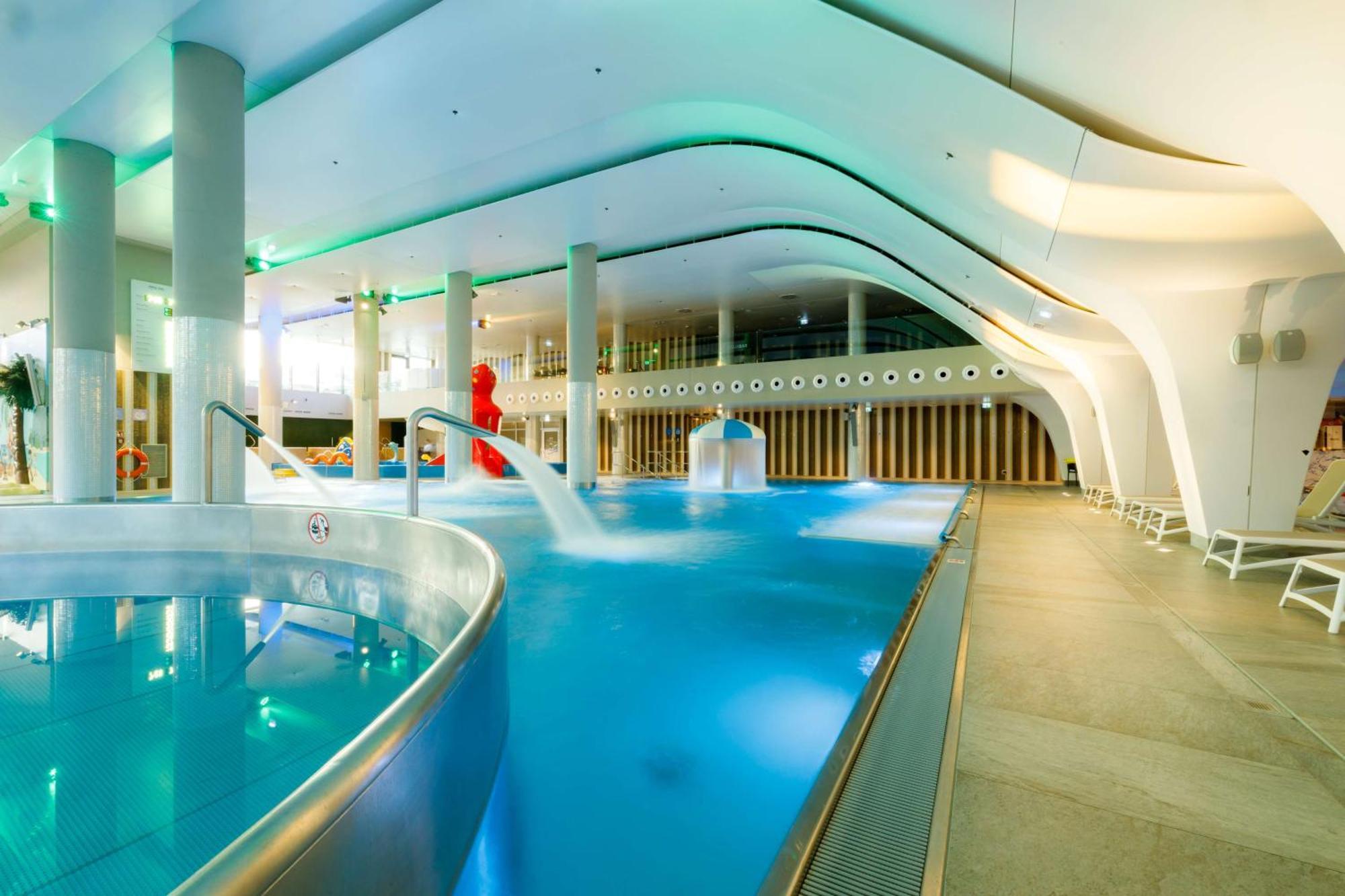 Radisson Blu Resort Świnoujście מראה חיצוני תמונה The photo shows a modern indoor swimming pool area with an elegant design. The pool features curved edges and is filled with clear, blue water. There are various amenities, such as jets for relaxation and possibly seating areas along the edges. The l
