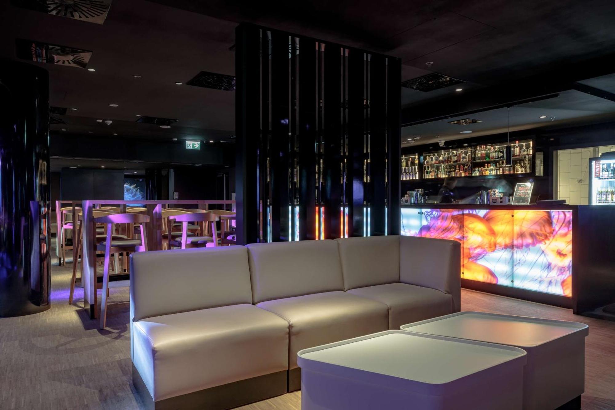 Radisson Blu Resort Świnoujście מראה חיצוני תמונה The photo depicts a modern interior space, possibly a lounge or bar. There are sleek, minimalistic furniture pieces, including a large, curved sofa and contemporary coffee tables. The lighting is dim, with a blend of colorful ambient lights illuminat