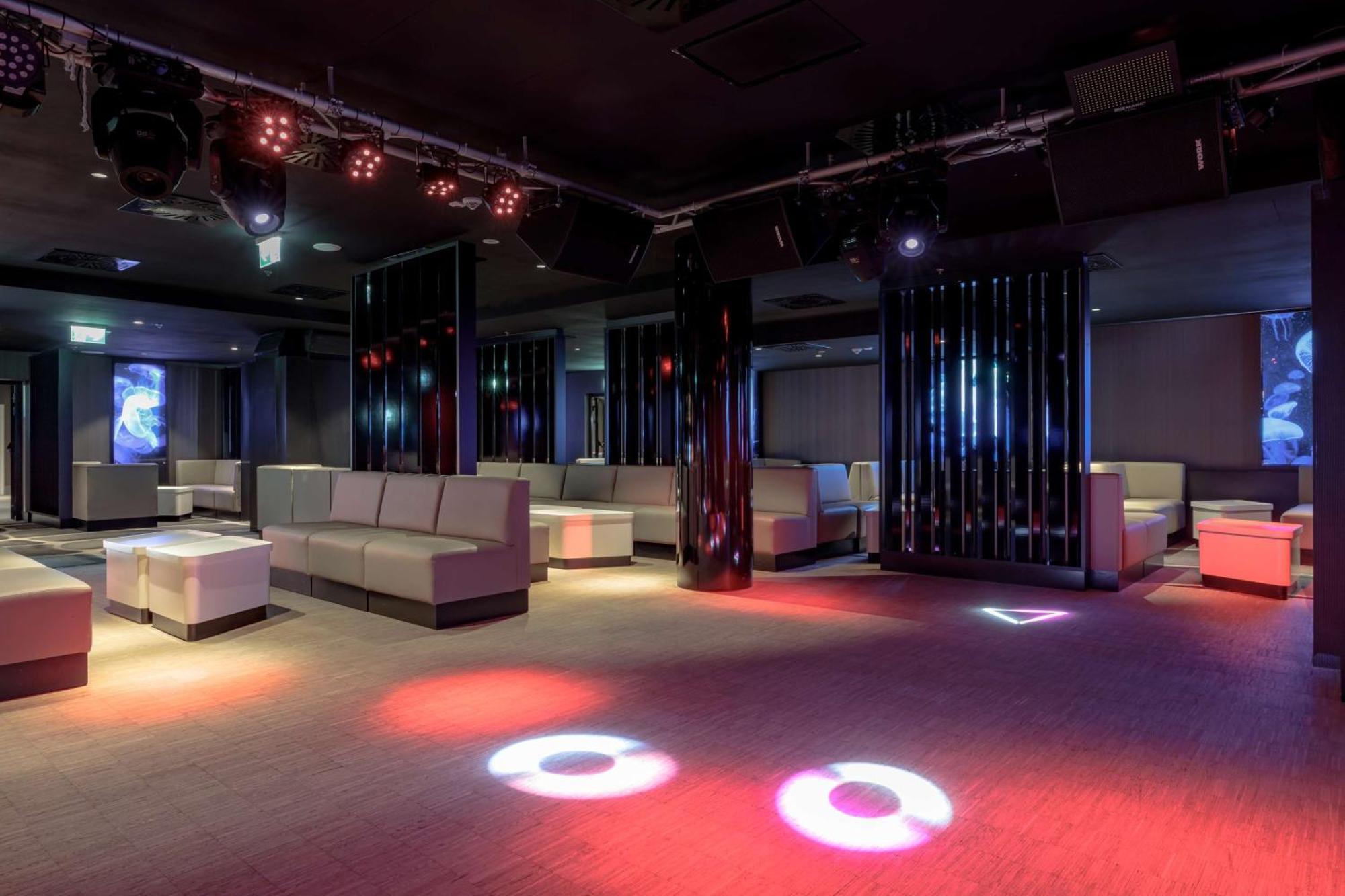 Radisson Blu Resort Świnoujście מראה חיצוני תמונה The photo depicts a modern nightclub interior, featuring a spacious layout with sleek, minimalist seating arrangements. The room has plush seating along the walls, and the floor is illuminated with circular lights in varying colors, creating a vibran
