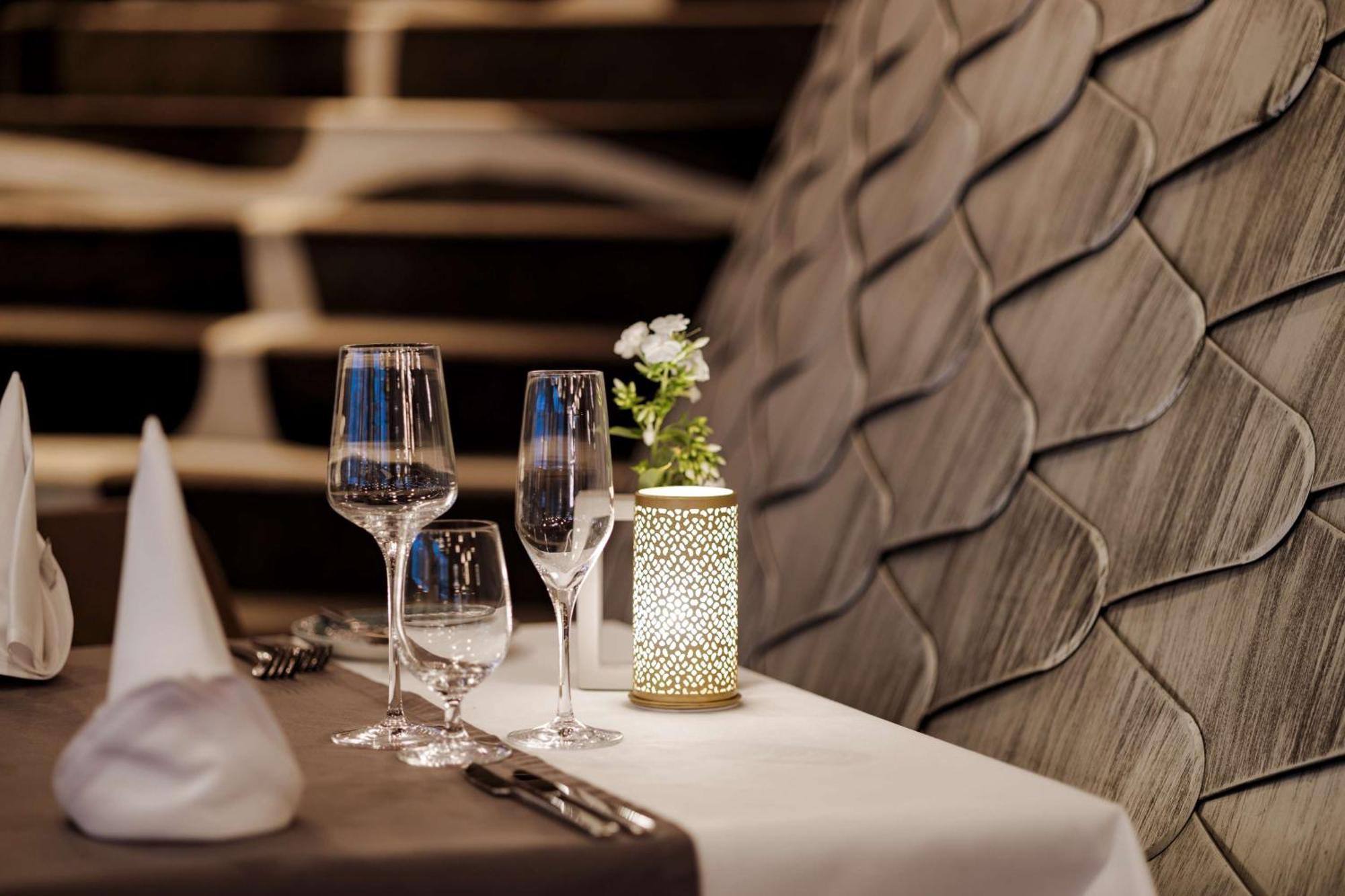 Radisson Blu Resort Świnoujście מראה חיצוני תמונה The photo shows a beautifully arranged table setting in a restaurant. There are two elegant wine glasses and a smaller glass, likely for water, placed on a crisp white tablecloth. A decorative lantern with intricate designs holds a small flower arran