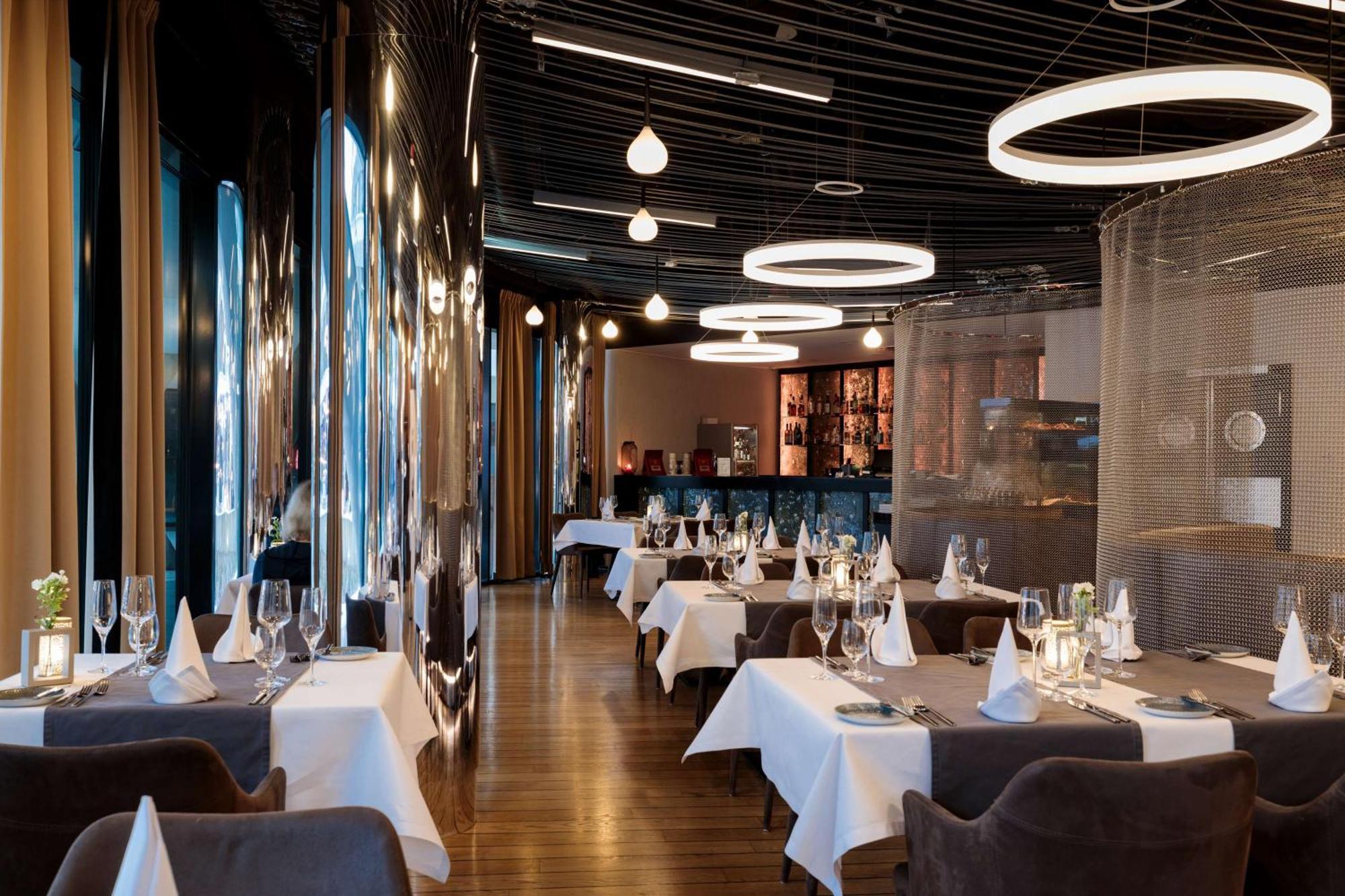 Radisson Blu Resort Świnoujście מראה חיצוני תמונה The photo shows the interior of a modern restaurant. It features elegantly set tables with white tablecloths and neatly arranged glassware. The design includes a sleek, contemporary aesthetic with dark walls and interesting lighting, including circul