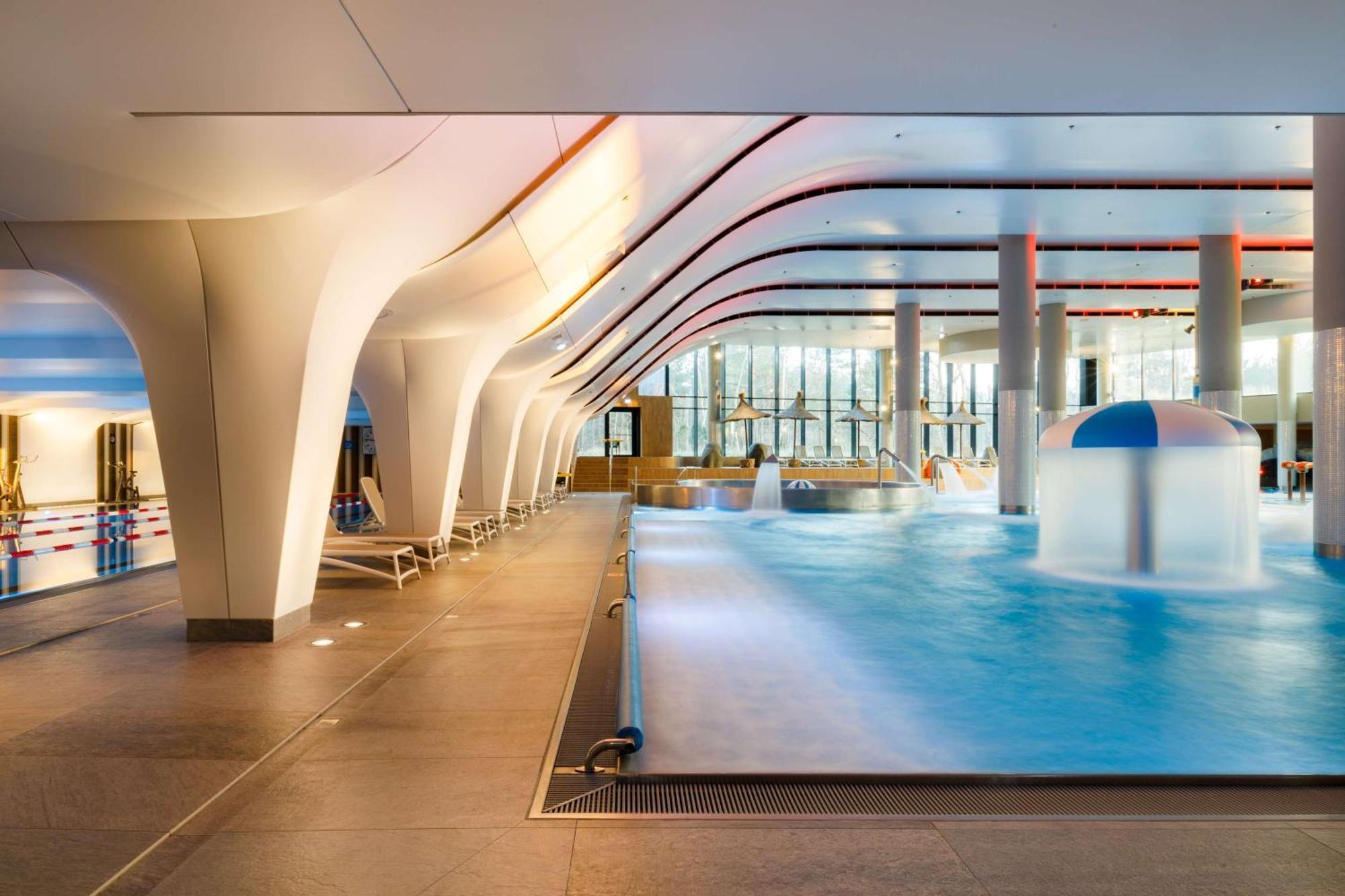 Radisson Blu Resort Świnoujście מראה חיצוני תמונה The photo shows an indoor swimming pool area with a modern architectural design. The space features large windows allowing natural light to enter, and the interior has smooth, flowing lines in the ceiling and columns. The pool has a light blue water 