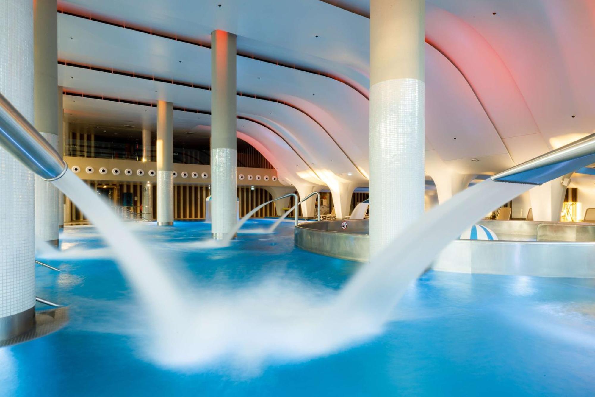 Radisson Blu Resort Świnoujście מראה חיצוני תמונה The photo depicts an indoor swimming pool area characterized by modern architecture. The pool is filled with clear blue water, and there are several columns supporting the ceiling. Water features, such as jets or fountains, are seen creating flowing 