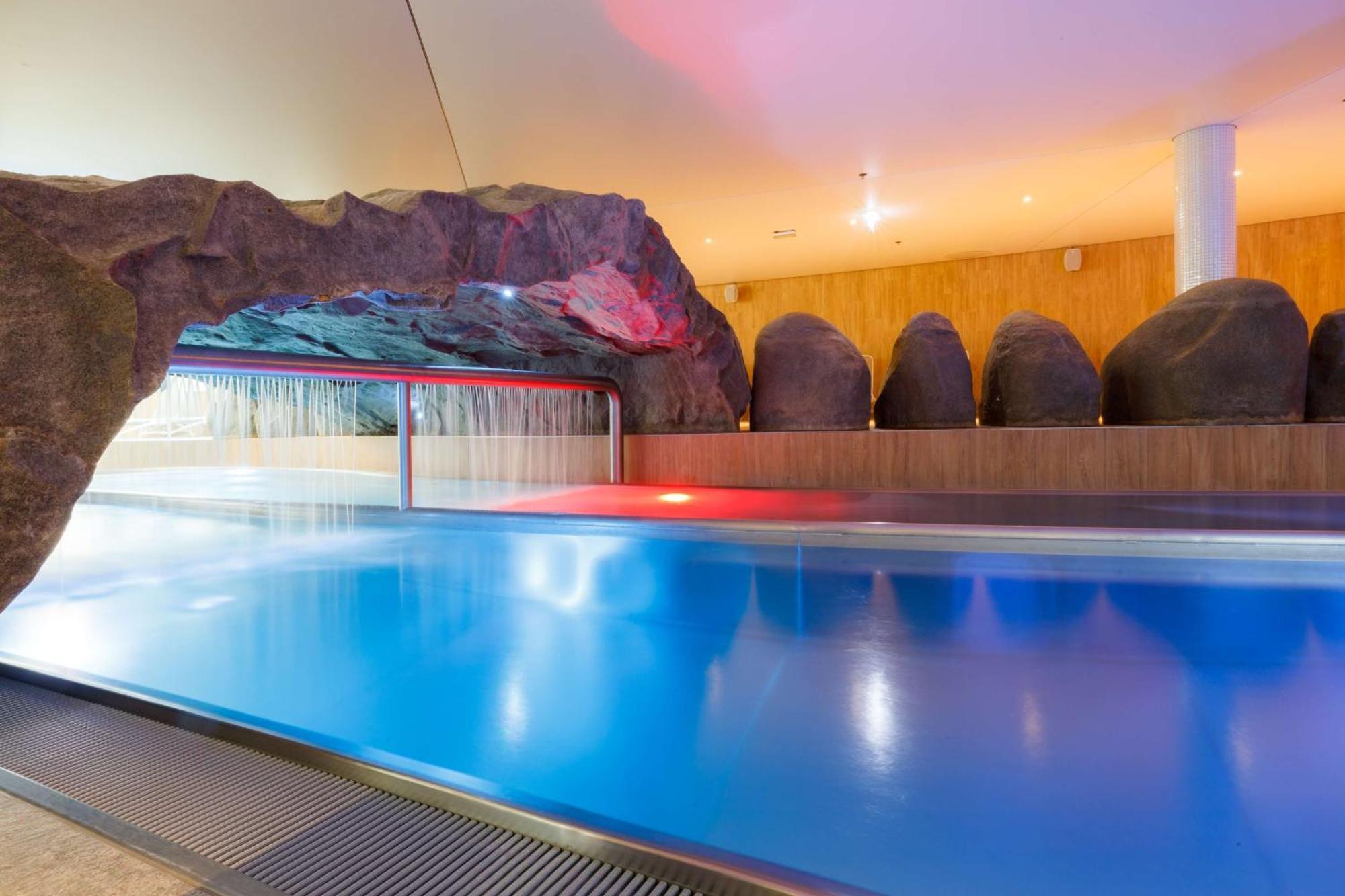 Radisson Blu Resort Świnoujście מראה חיצוני תמונה The photo shows a serene indoor swimming pool area. The pool has clear blue water, and there is a distinctive rock formation that resembles a cave on one side. Soft lighting enhances the atmosphere, casting a gentle glow across the space. In the back