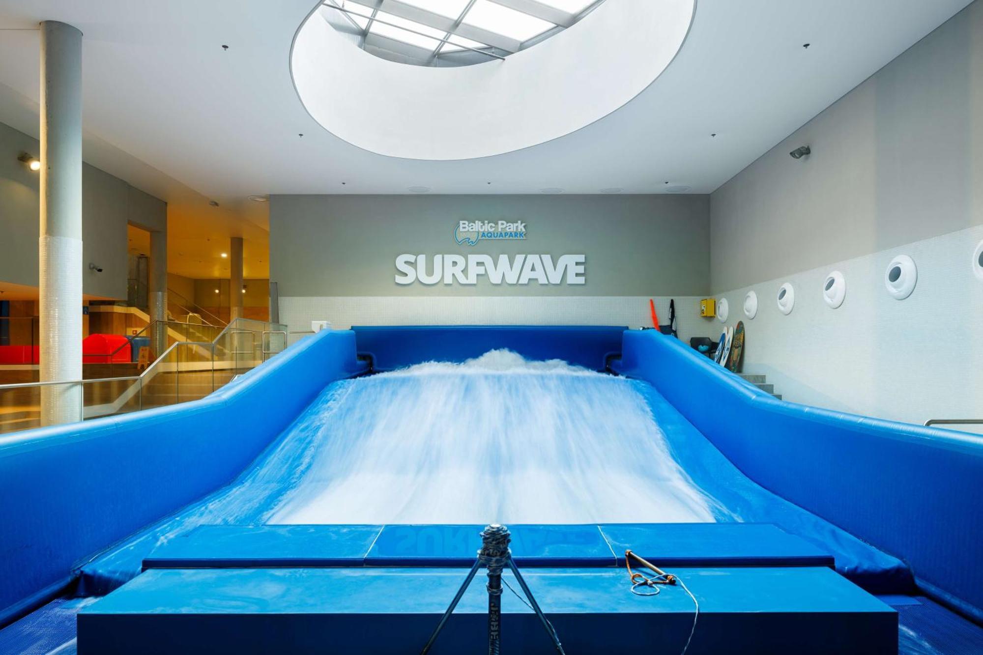 Radisson Blu Resort Świnoujście מראה חיצוני תמונה The photo shows an indoor surfing attraction called "Surfwave." It features a large blue ramp with water flowing down it, creating a wave-like effect for surfing. Above the ramp, there is a sign that says "SURFWAVE." The area appears well-lit and mod